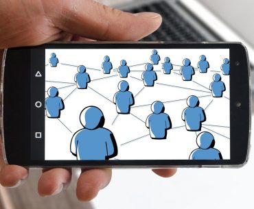 A hand holding a smartphone containing an image of multiple blue figures connected in a web.