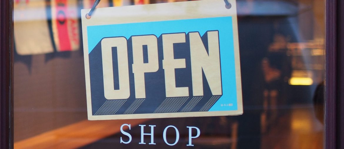 An open sign hangs from a glass door to a business directly above the word “shop.”