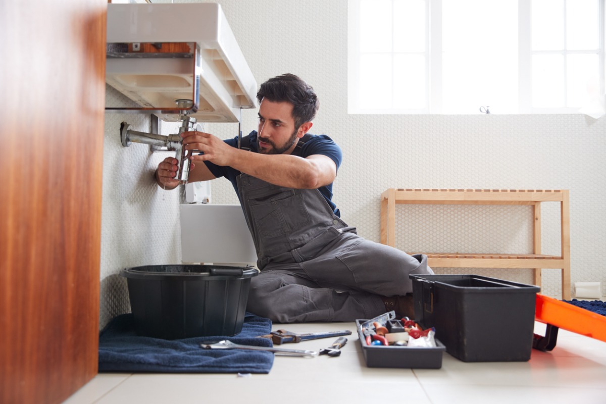  A professional and trusted home repair handyman is fixing a sink in a bathroom.