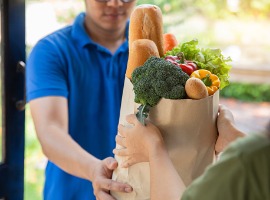deliver man in blue uniform handling bag of food fruit vegetable give to female customer in