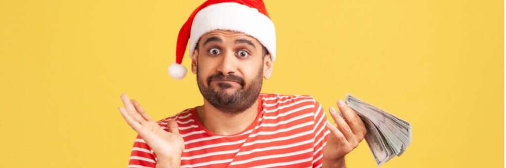 puzzled confused man with beard in red santa claus hat holding cash in hands dont know how to