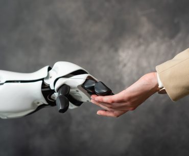 The hand of a person wearing a business suit touching fingers with a robotic hand.