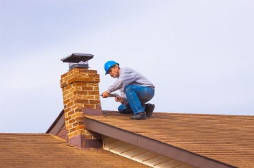 contractor builder with blue hardhat on the roof caulking chimney picture