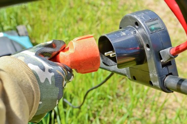 gloved hand with electric cable and plug connects the lawn mower to picture