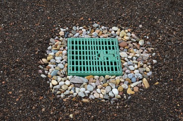 green gutter used for drainage surrounded by pea gravel