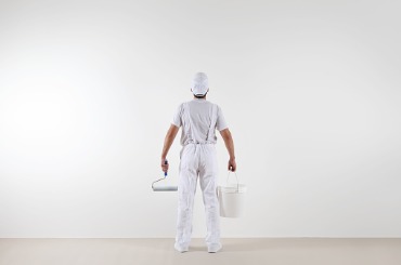 rear view of painter man looking at blank wall with paint roller and picture