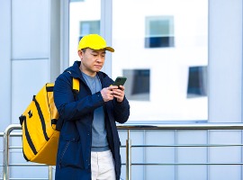 asian male food courier using mobile using mobile phone app on smartphone while standing city