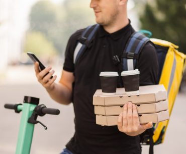 courier delivering food and hot drinks outside guy using smartphone at city street