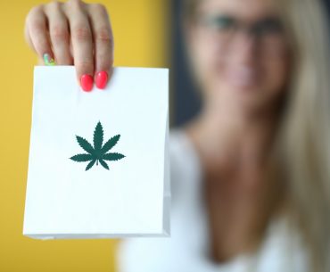 female hand holds paper bag with an image of marijuana symbol closeup