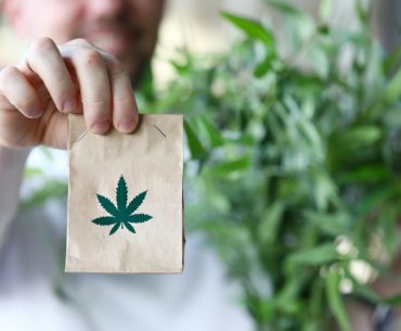 male hand hold paper packet with marijuana symbol closeup background