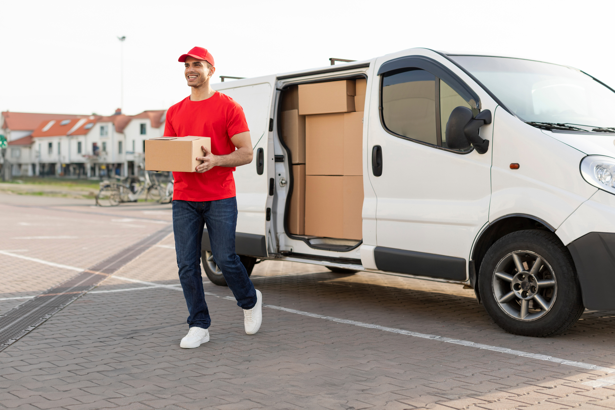 Smiling delivery man in uniform carries package from his white van, delivering parcel to customer, walking outdoors